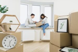 young couple sitting window sill unpacking cardboard boxes